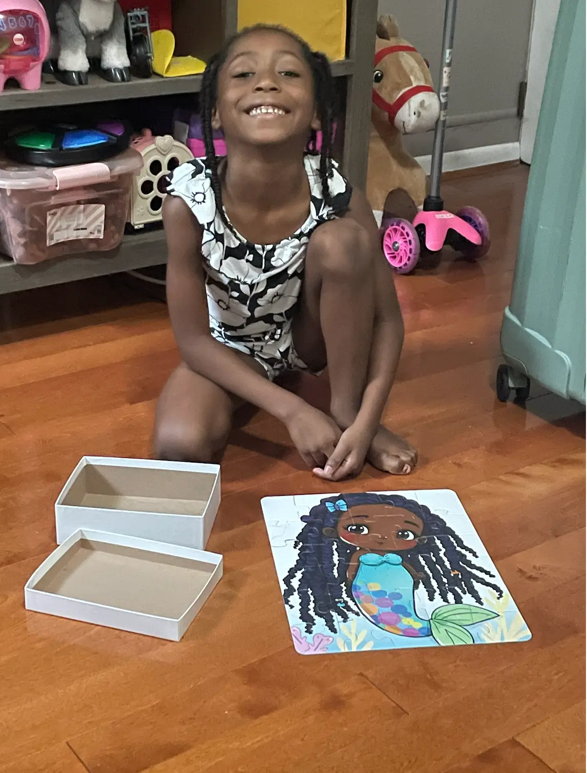 Augustine smiling on the floor beside the finished original mermaid puzzle, the most recent photo